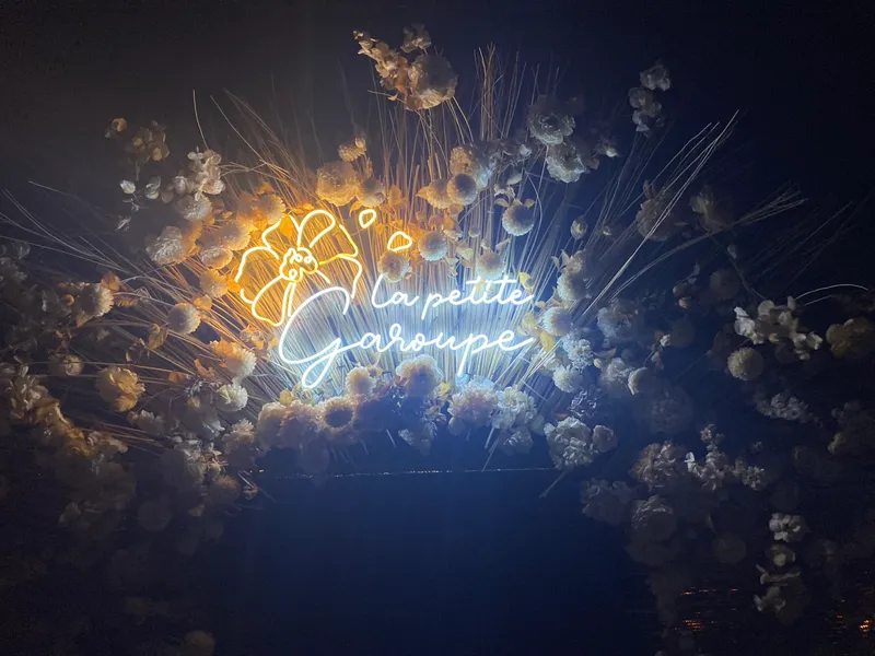 A photo of the sign at the entrance to La Petite Garoupe restaurant, Antibes. The letters are in neon and the sign is surrounded by flowers.