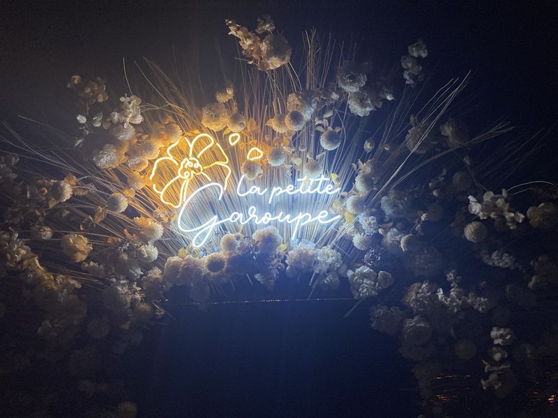 A photo of the sign at the entrance to La Petite Garoupe restaurant, Antibes. The letters are in neon and the sign is surrounded by flowers.