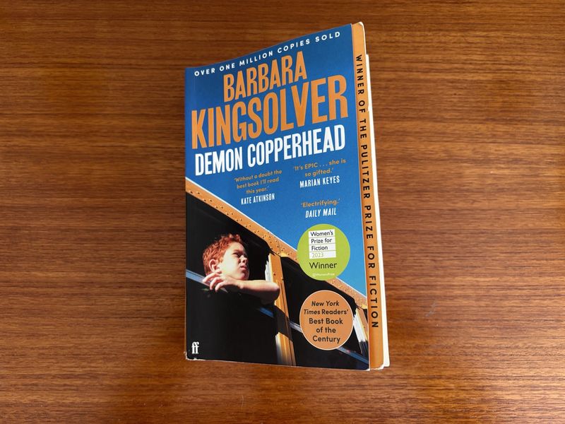 A paperback copy of Barbara Kingsolver’s book “Demon Copperhead” sitting atop a wooden table